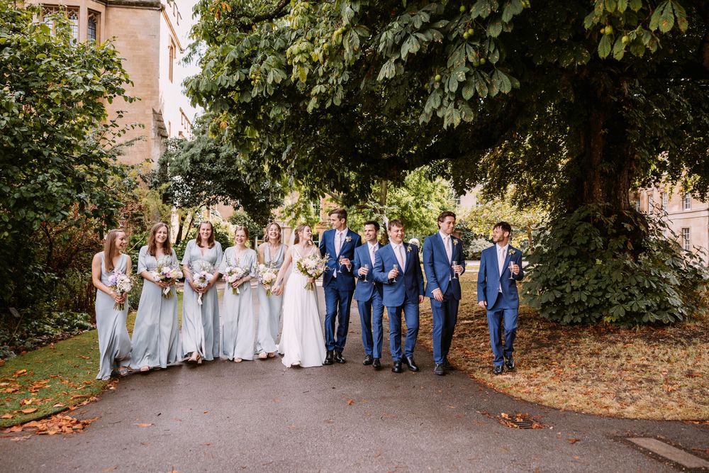Bridal party stands together on autumn pathway with bridesmaids in gray and groomsmen in navy blue.