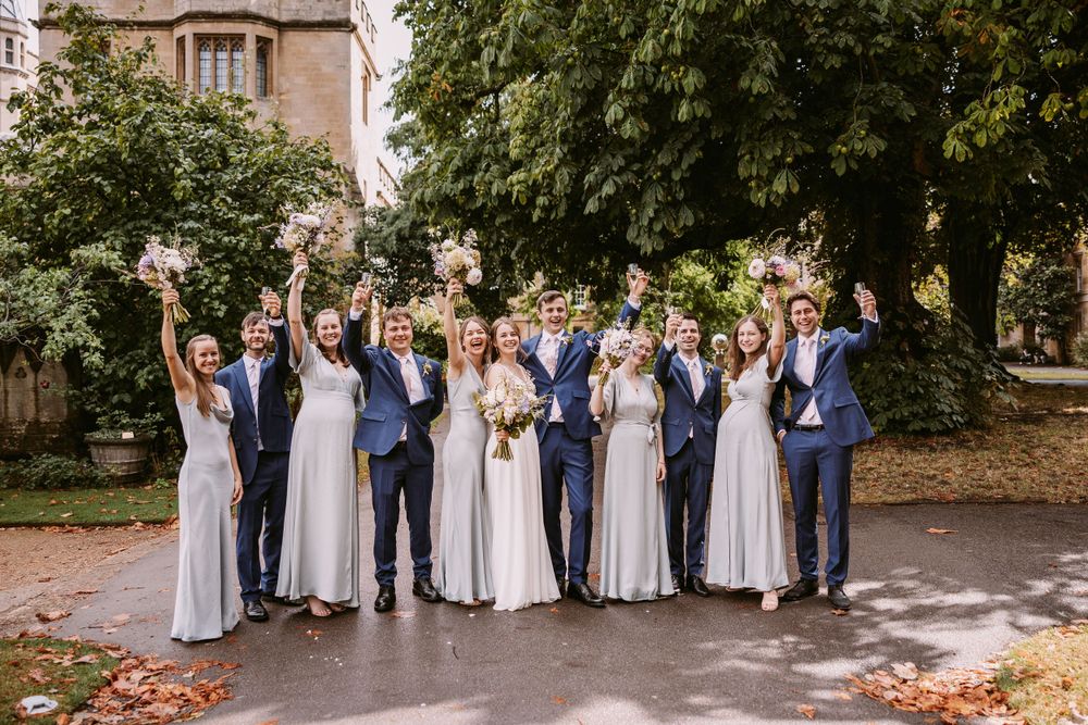 Wedding group poses cheerfully outdoors with coordinated blue and gray attire.