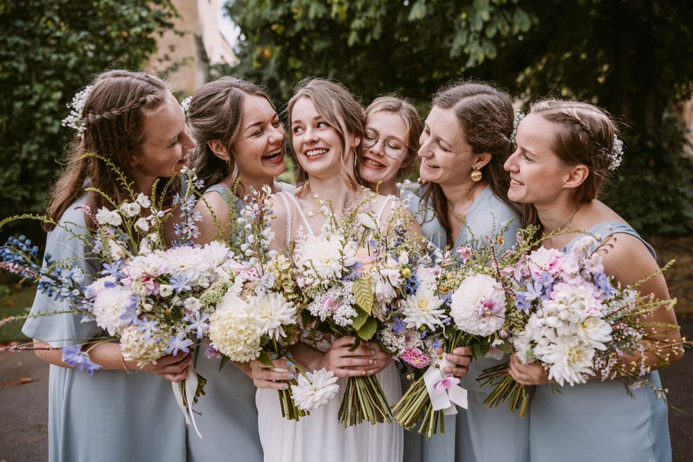 Bridal party holding elegant bouquets of pink and white flowers laugh together outdoors.