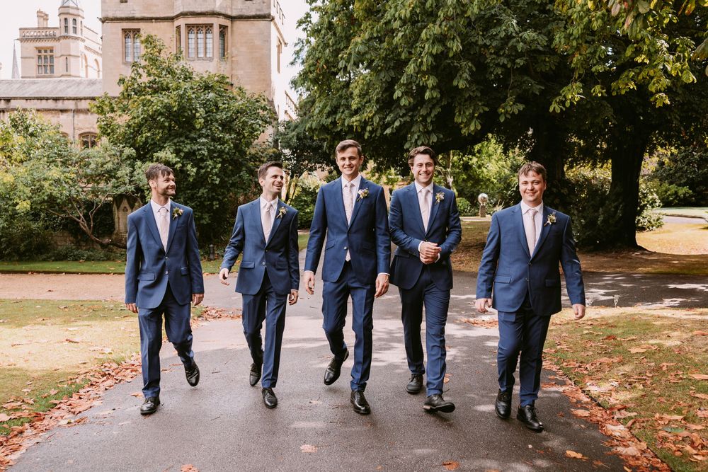 Groomsmen stride confidently along autumn pathway in coordinated navy suits.