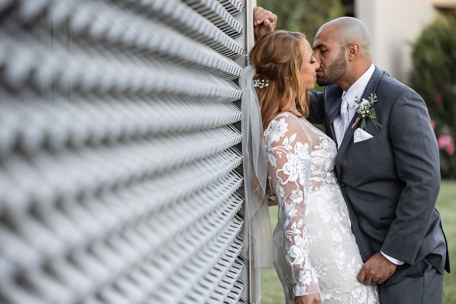 A romantic wedding couple poses against a geometric wall in dramatic lighting.