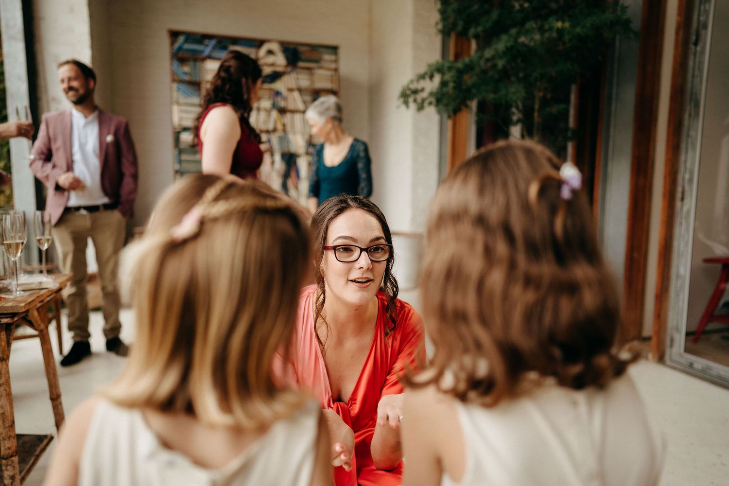 A gathering of people engaged in conversation at an indoor social event with natural lighting.