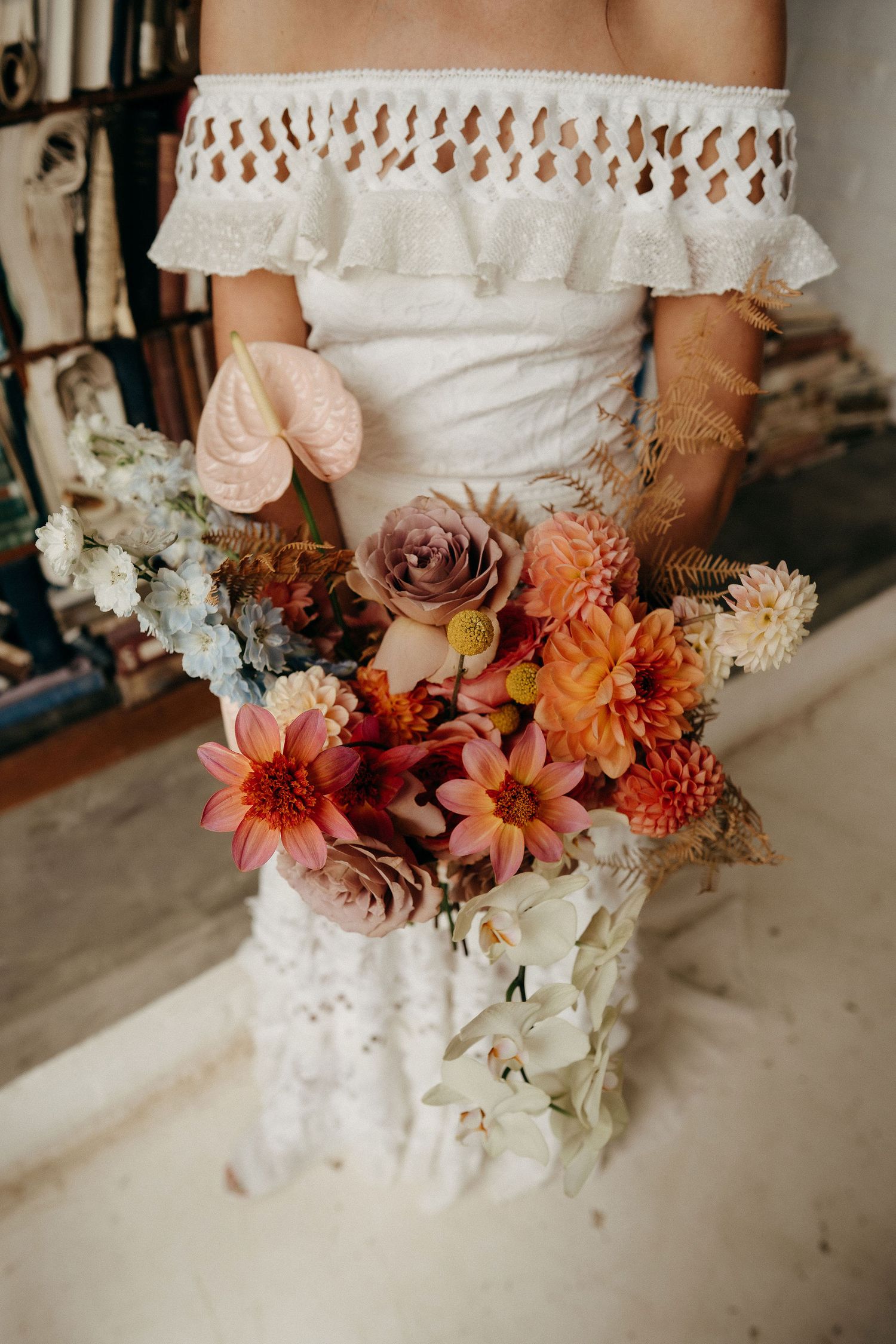 A bridal bouquet featuring peach and mauve roses, dahlias and mixed flowers against a white lace wedding dress.