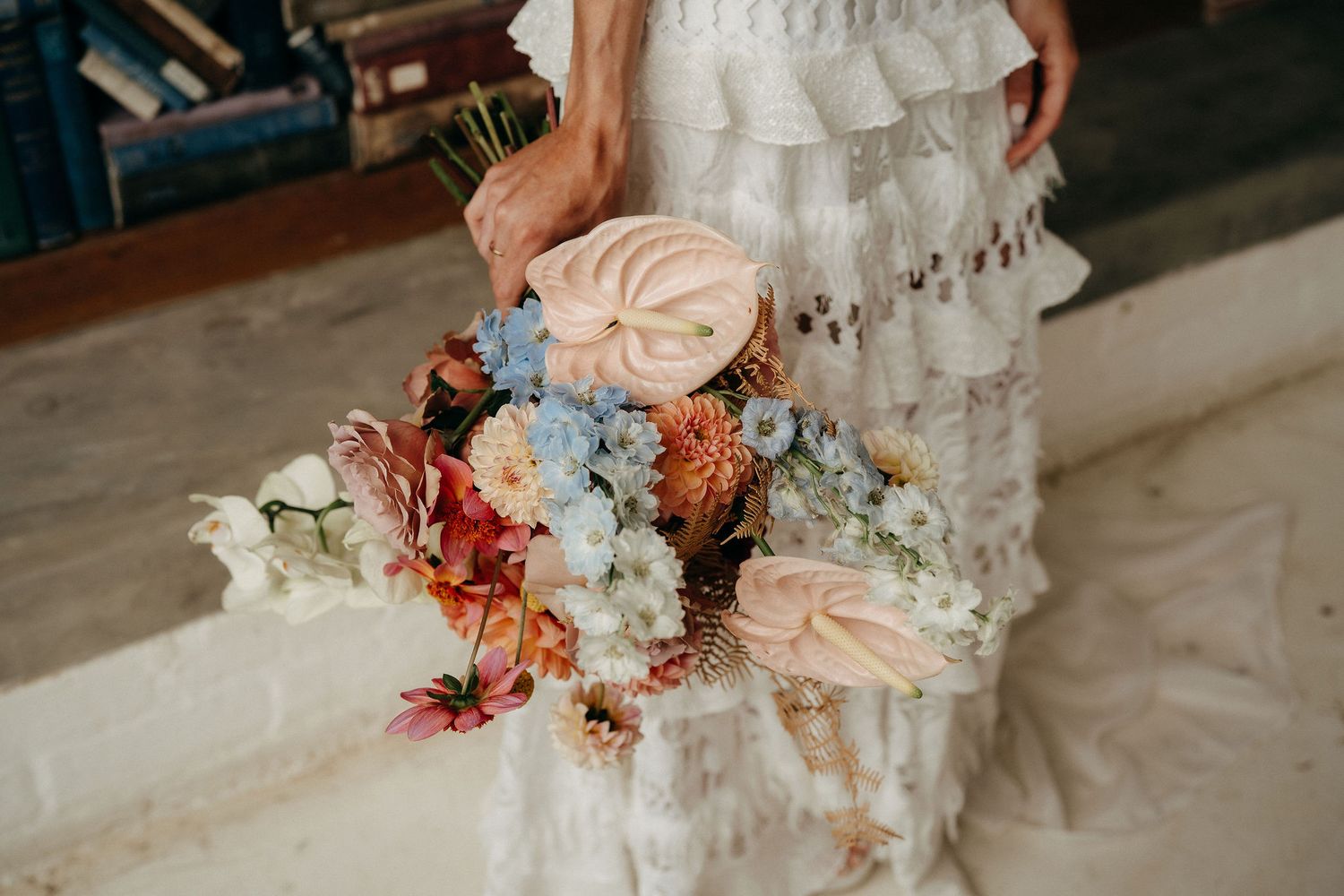 A romantic bridal bouquet featuring blush roses, coral blooms and white flowers held against a ruffled wedding dress.