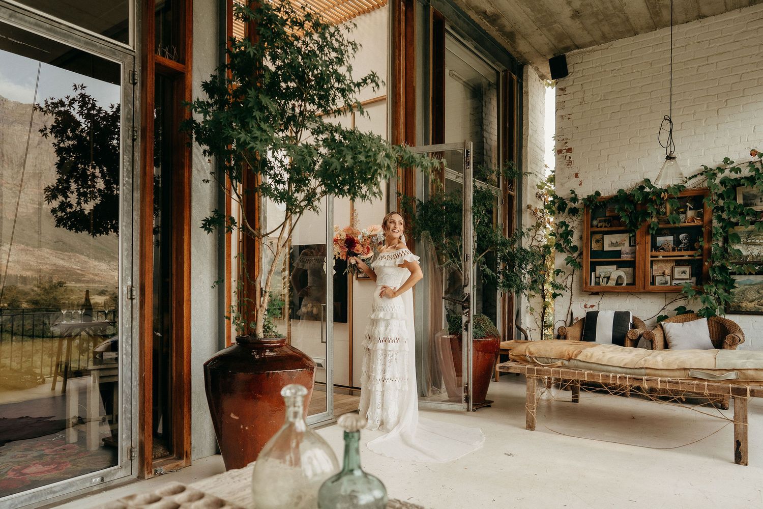 Cozy boho-style porch with potted plants, wooden furniture, and large glass windows creating an indoor-outdoor living space.