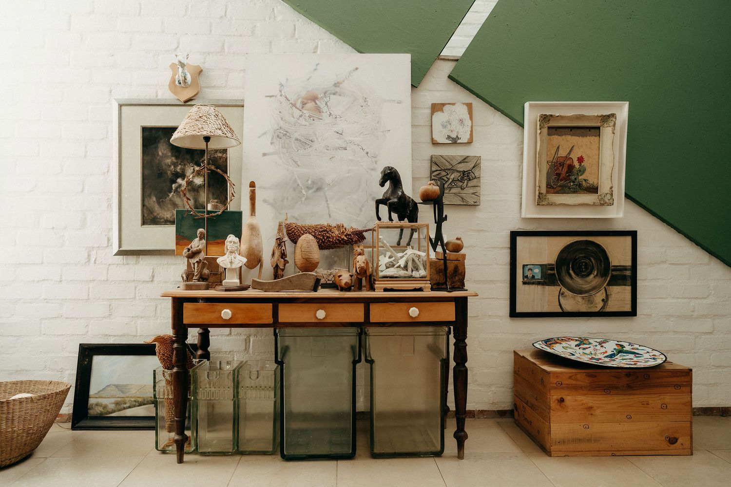 Vintage-style console table with rustic decor, framed artwork, and collected trinkets against white brick and green wall.