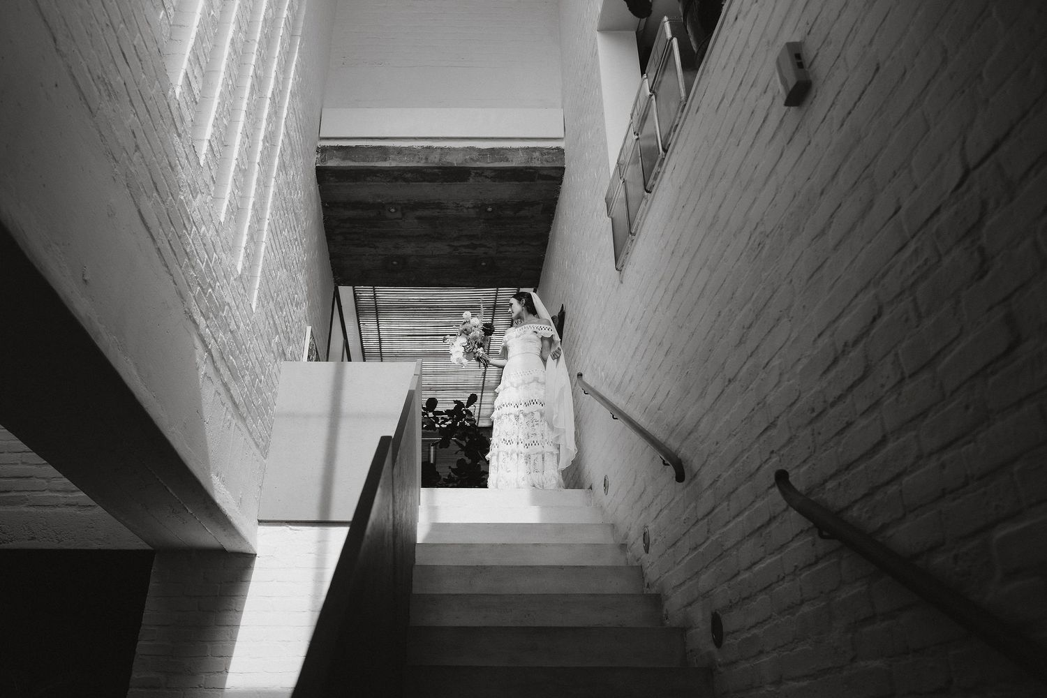 Black and white photograph showing wedding couple descending a modern staircase with white walls.