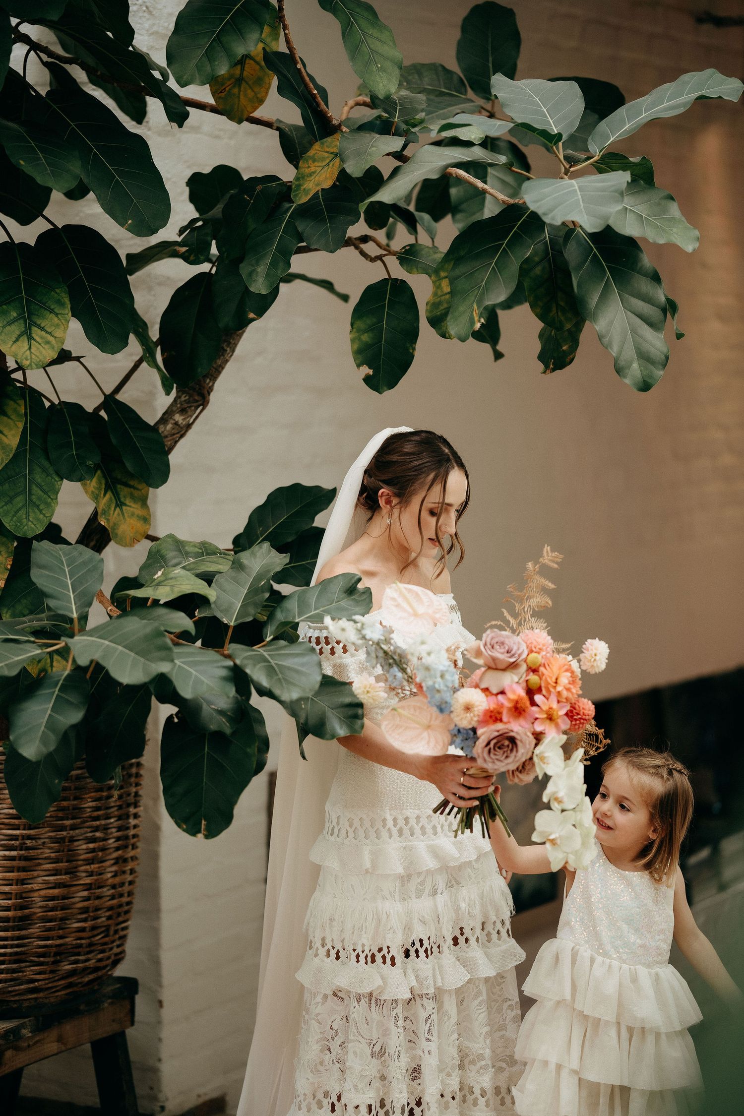 A lace wedding dress and flowing foliage frame this intimate moment under a fig tree with peach and pink florals.