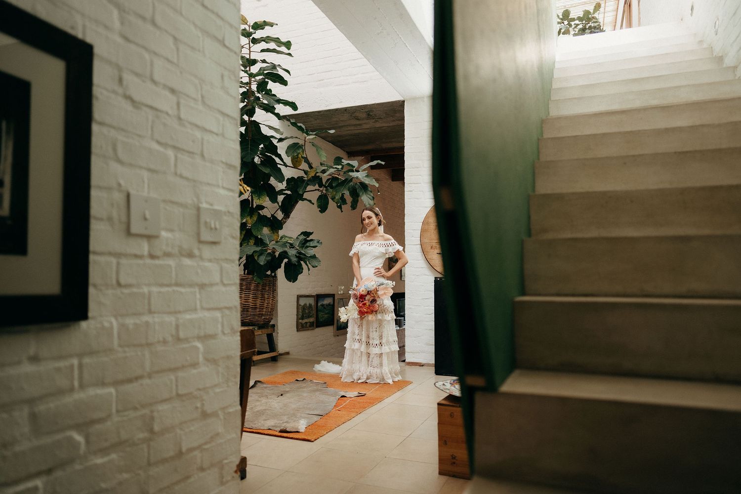 Interior view of hallway with white brick walls, orange runner rug, potted plant and staircase.