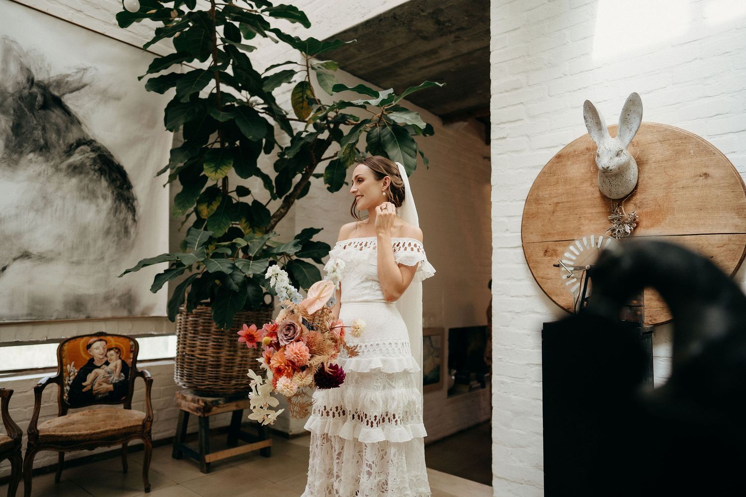A person in a vintage-style lace wedding dress stands in an elegantly decorated room with a mounted wall bunny decor.
