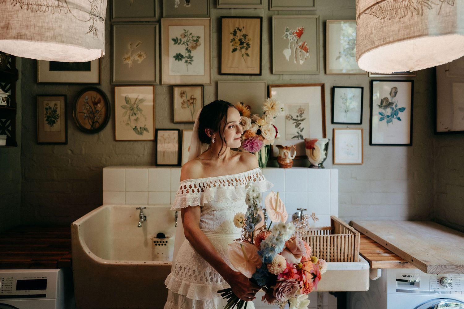 A vintage bathroom interior with botanical wall art and pendant lamps features bohemian style dress and floral arrangement.