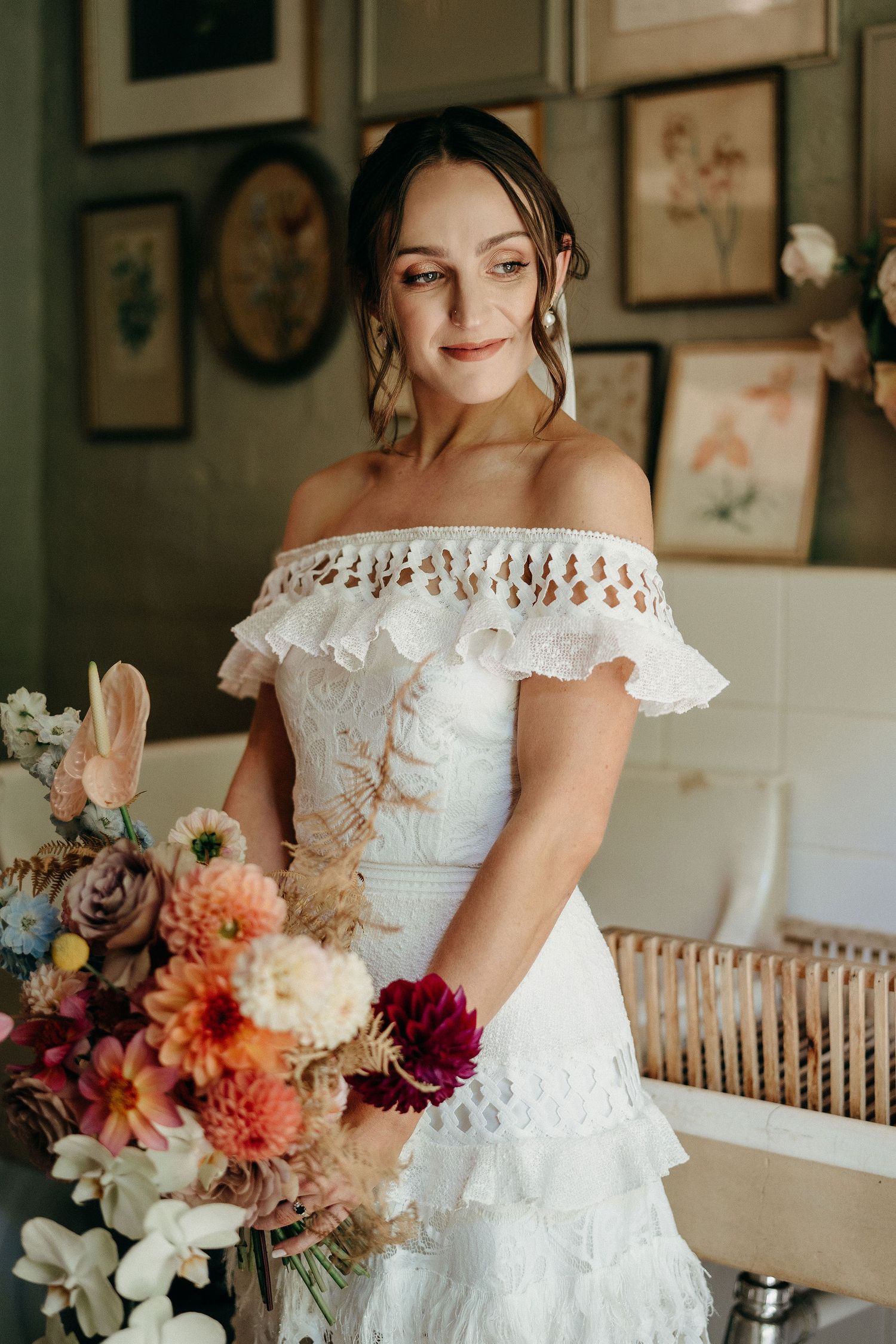A bride in a ruffled off-shoulder white wedding dress holds a vibrant autumn bouquet with dahlias and roses.