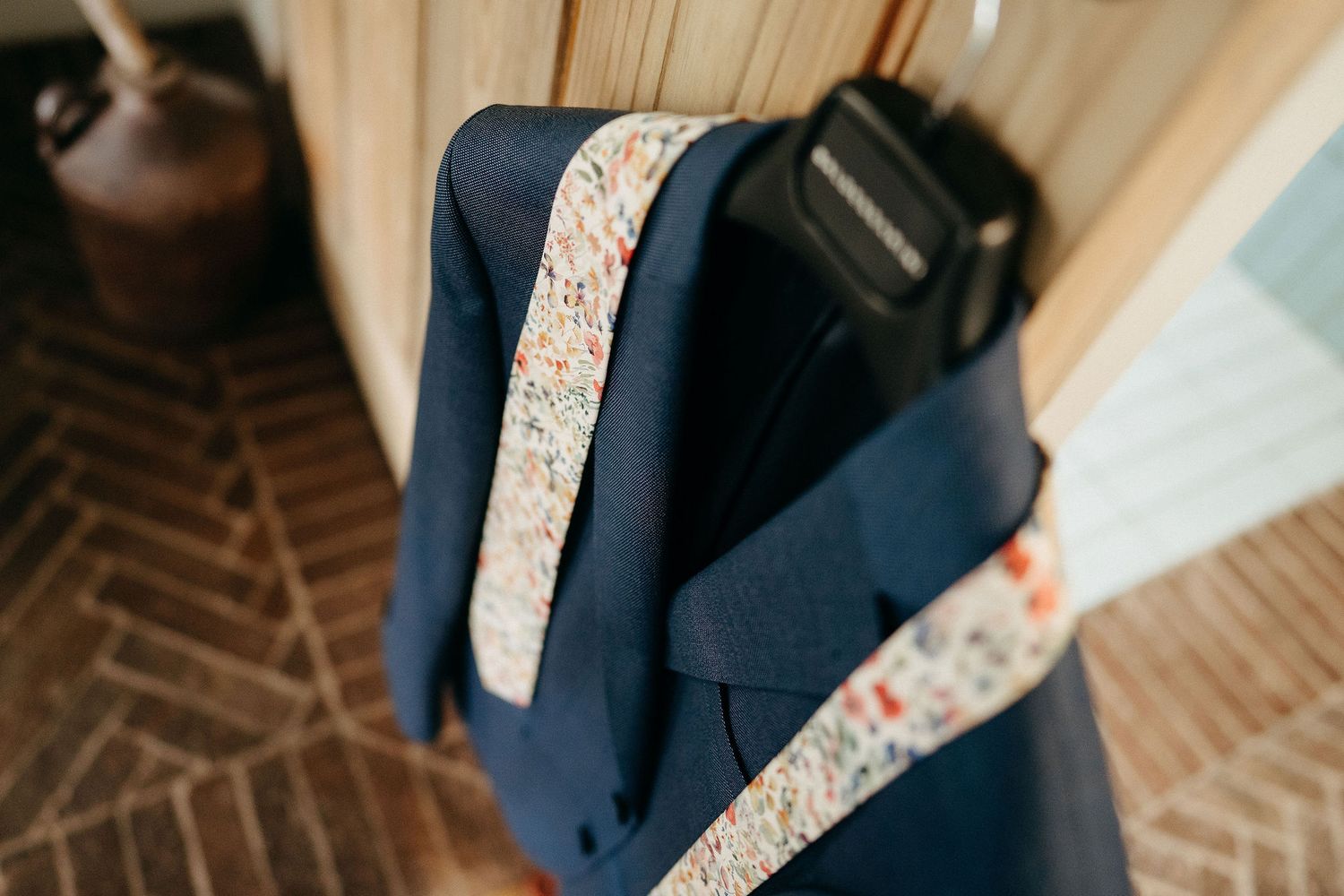 Navy blue suit jacket with decorative floral patterned trim hanging on wooden floor.