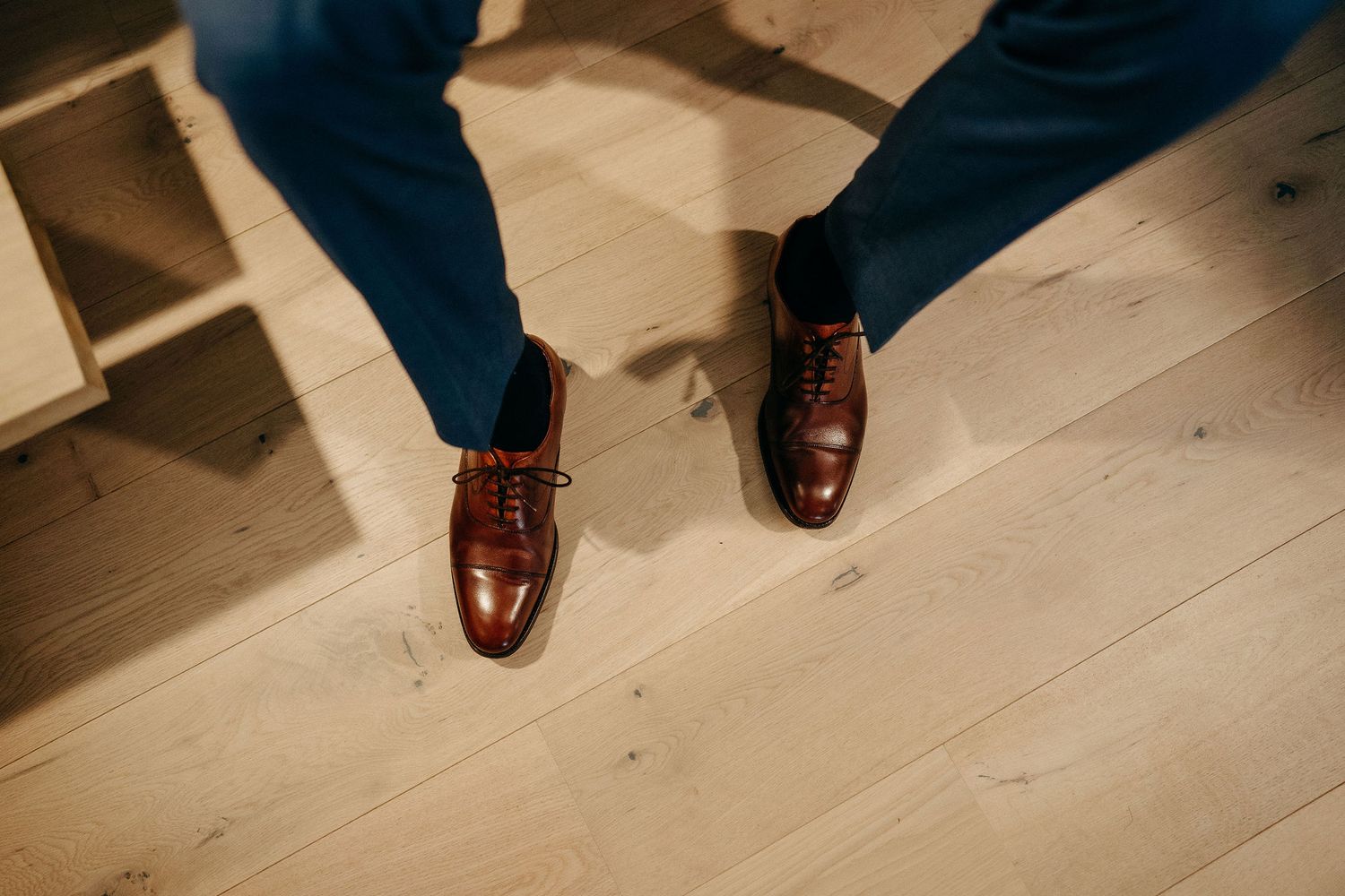 A close-up view of polished brown leather dress shoes on light wooden flooring.