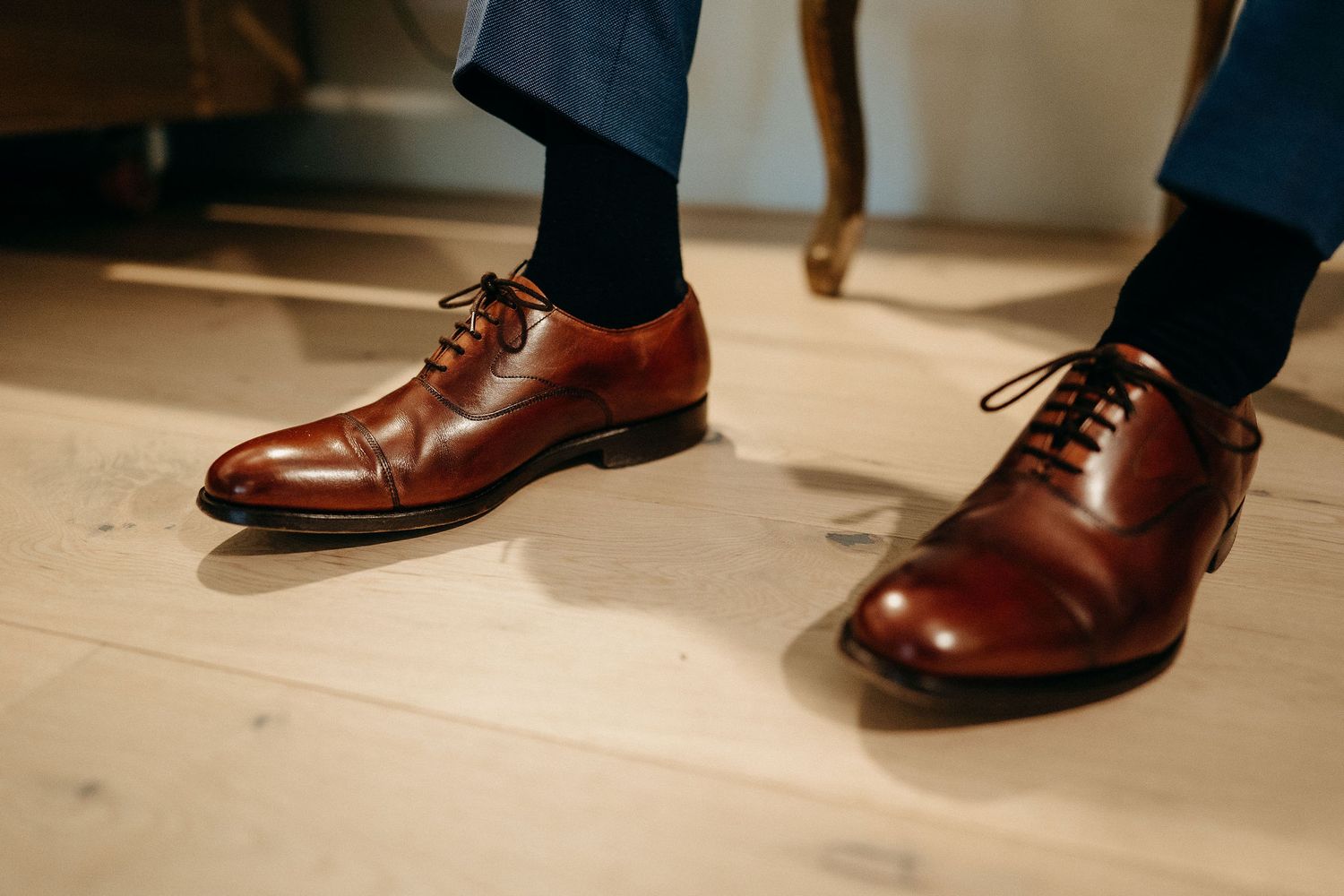 Close-up view of polished brown leather oxford dress shoes with dark navy dress pants.