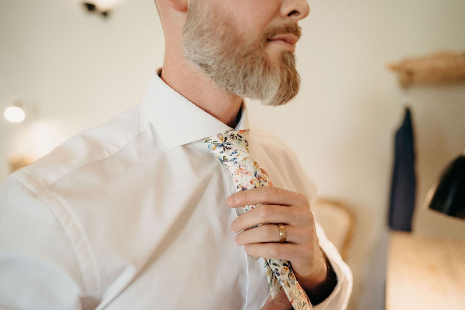 Close-up view of someone in a crisp white dress shirt adjusting a floral-patterned necktie.