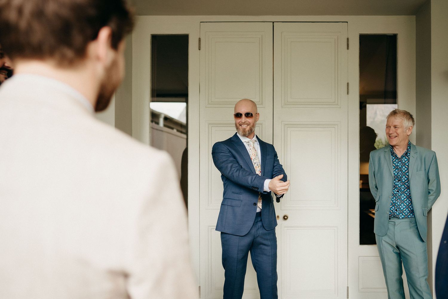 Three people stand in a doorway having an informal conversation before a wedding ceremony.
