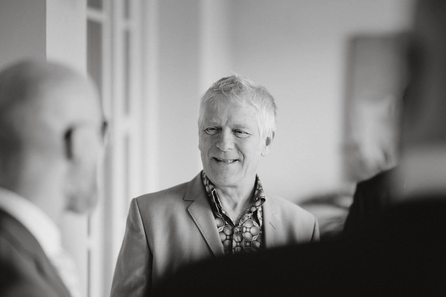 A candid black and white photo of a person smiling during what appears to be a social gathering.