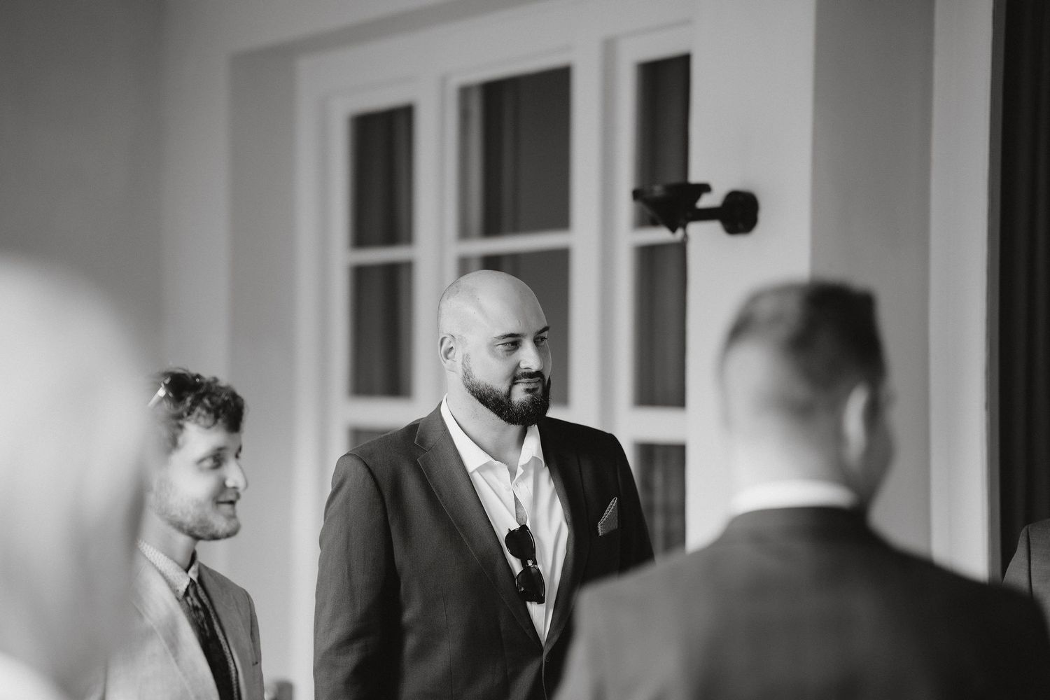 A candid black and white photo of groomsmen having a conversation before a wedding ceremony.