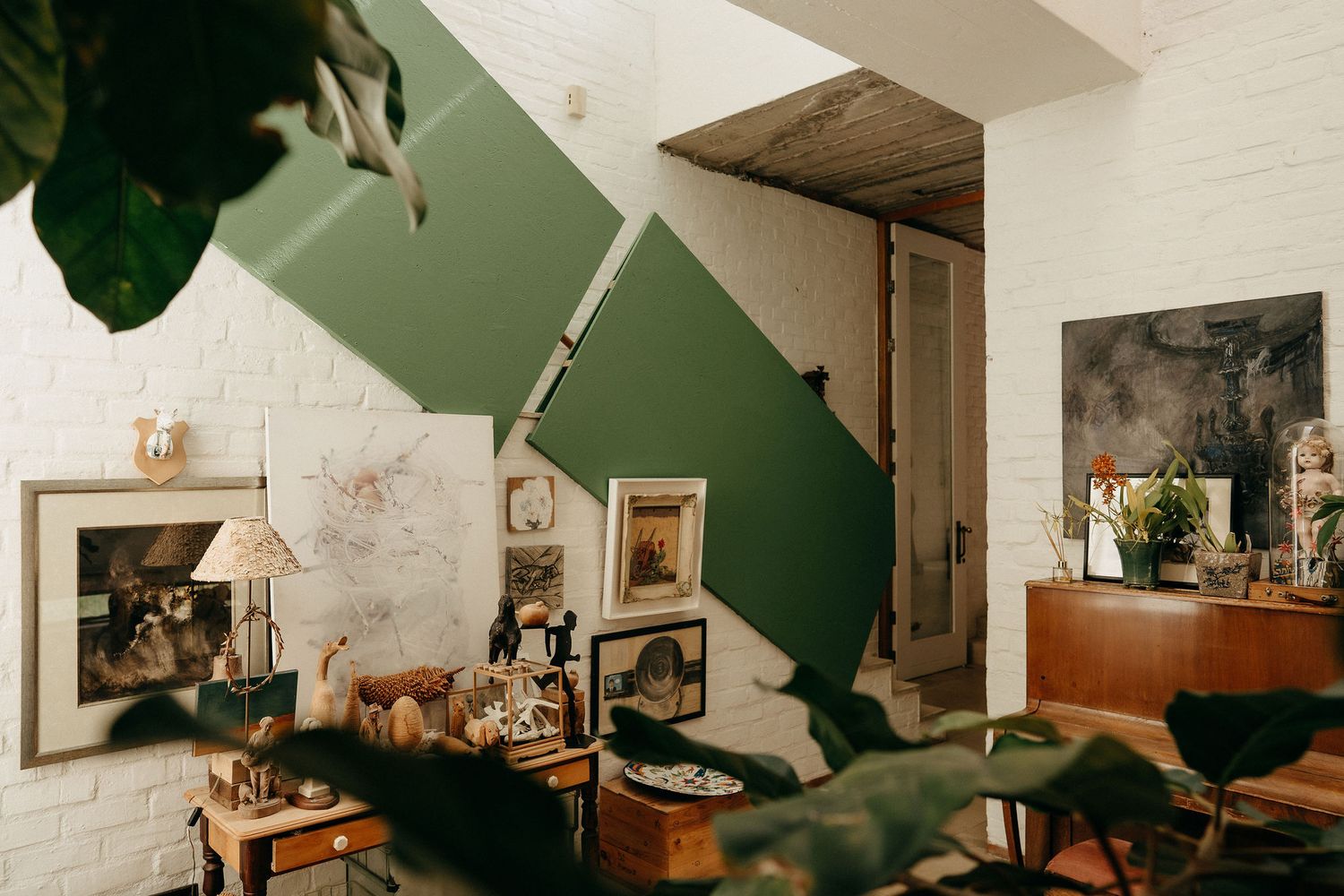 A cozy living room corner decorated with artwork and plants features dark green walls and vintage-style furniture and decor.