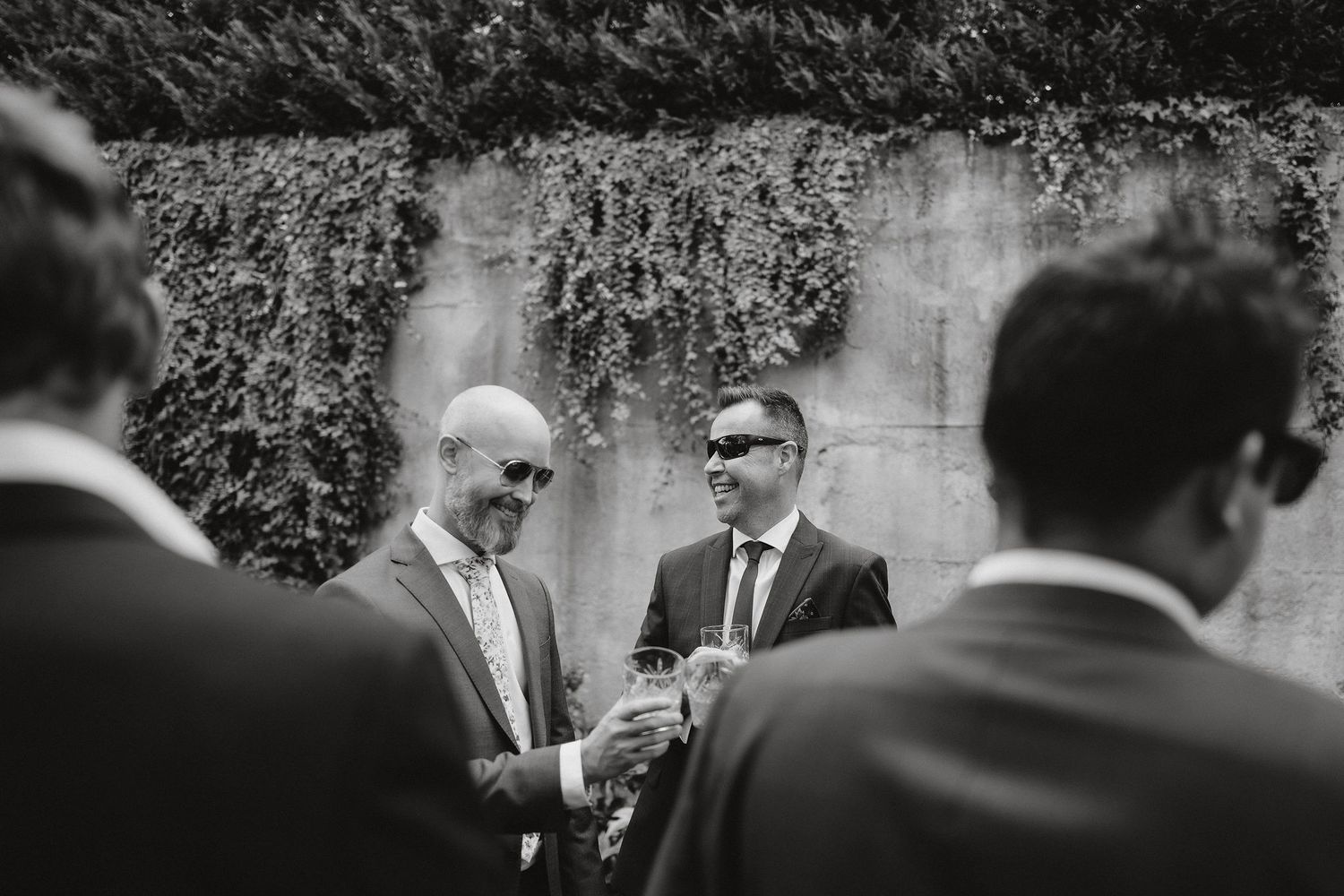 A black and white candid photograph of guests chatting and holding drinks at an outdoor garden party.
