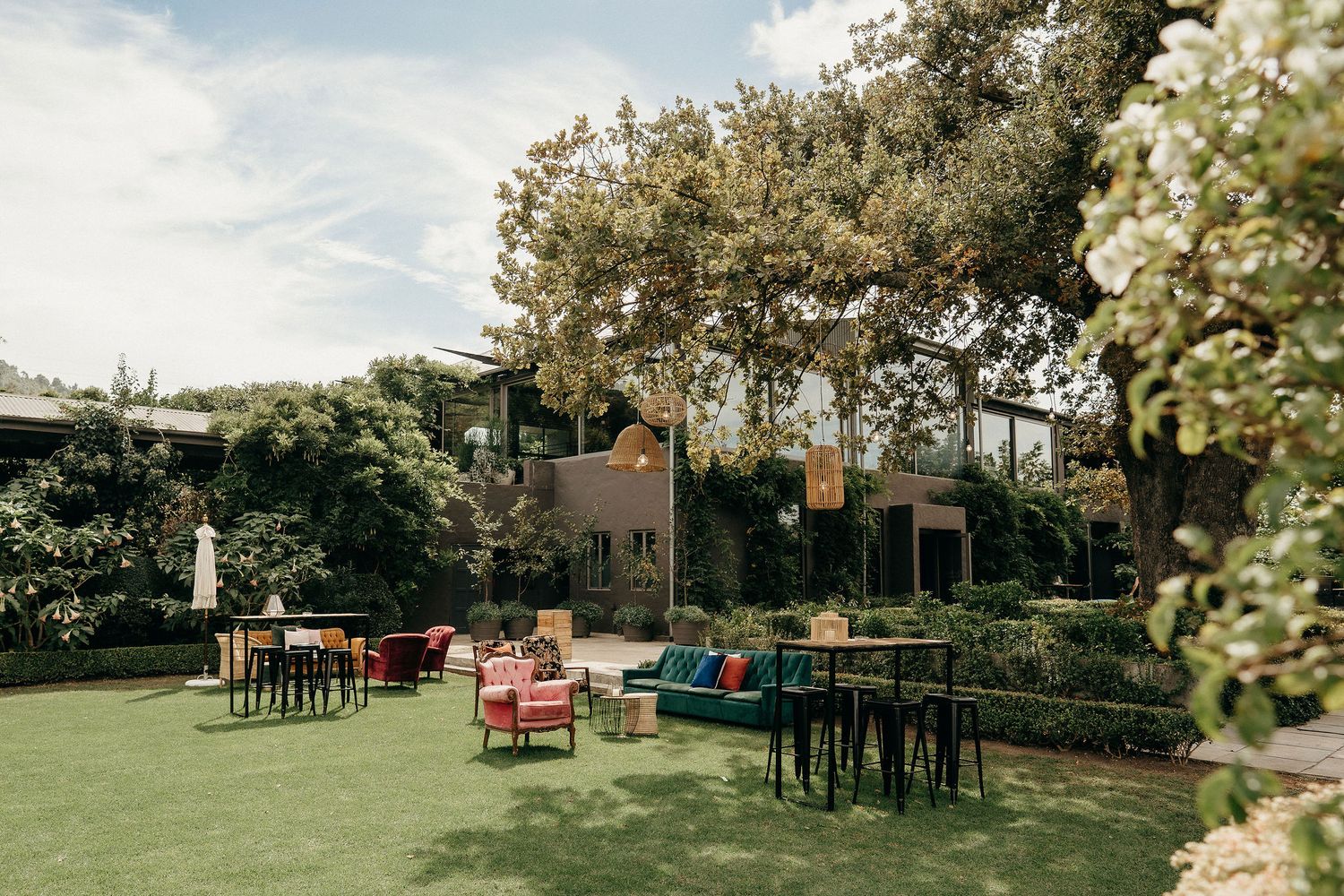 Outdoor garden event space with cozy seating arrangements, tables, and flowering trees under a cloudy sky.