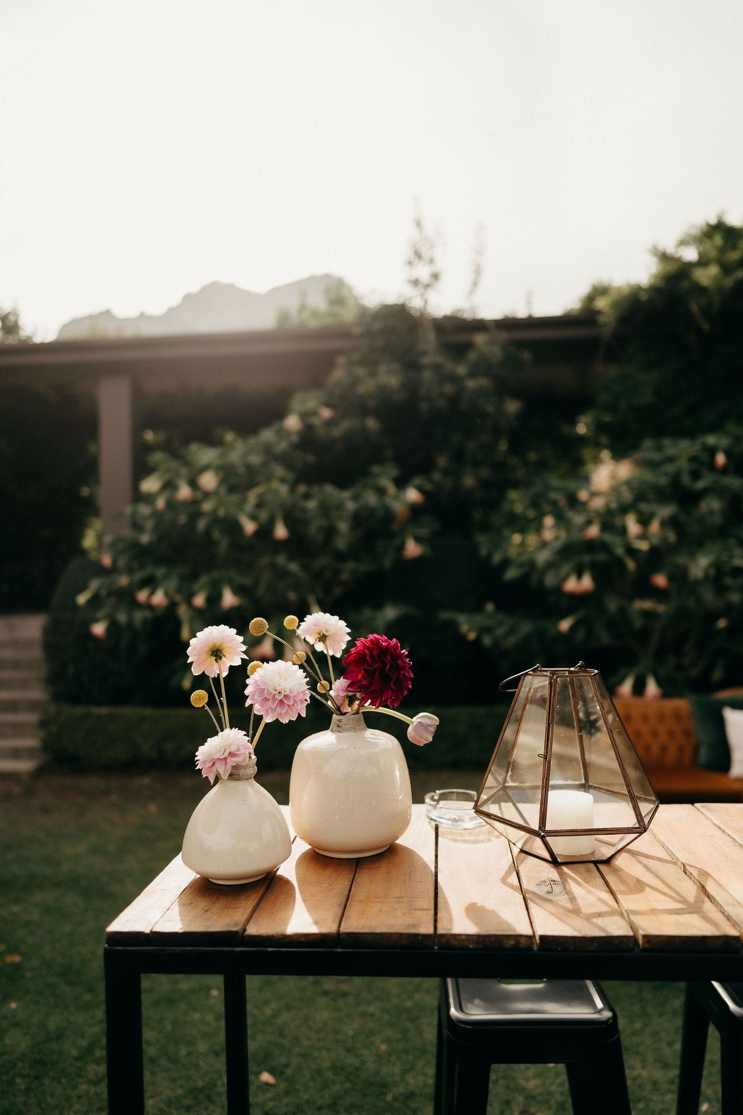 Rustic outdoor table setting with white vases of pink and red flowers and geometric lantern decor.