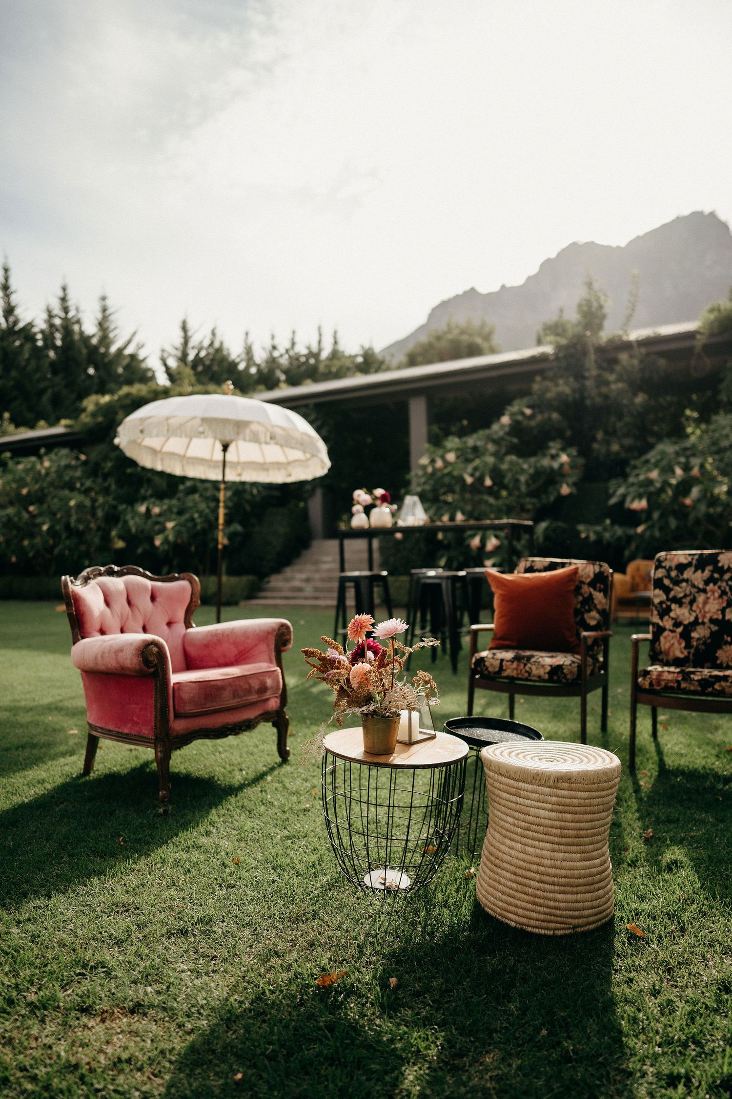Cozy outdoor lounge setup with vintage pink armchair, parasol, and decorative furniture on a grass lawn.