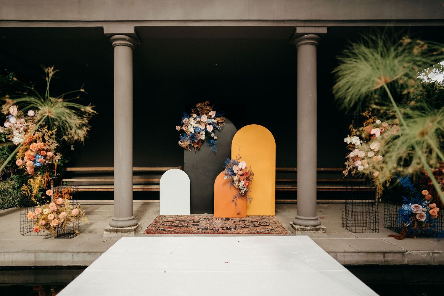 Modern wedding ceremony setup with cream and orange geometric backdrops and floral arrangements between white columns.