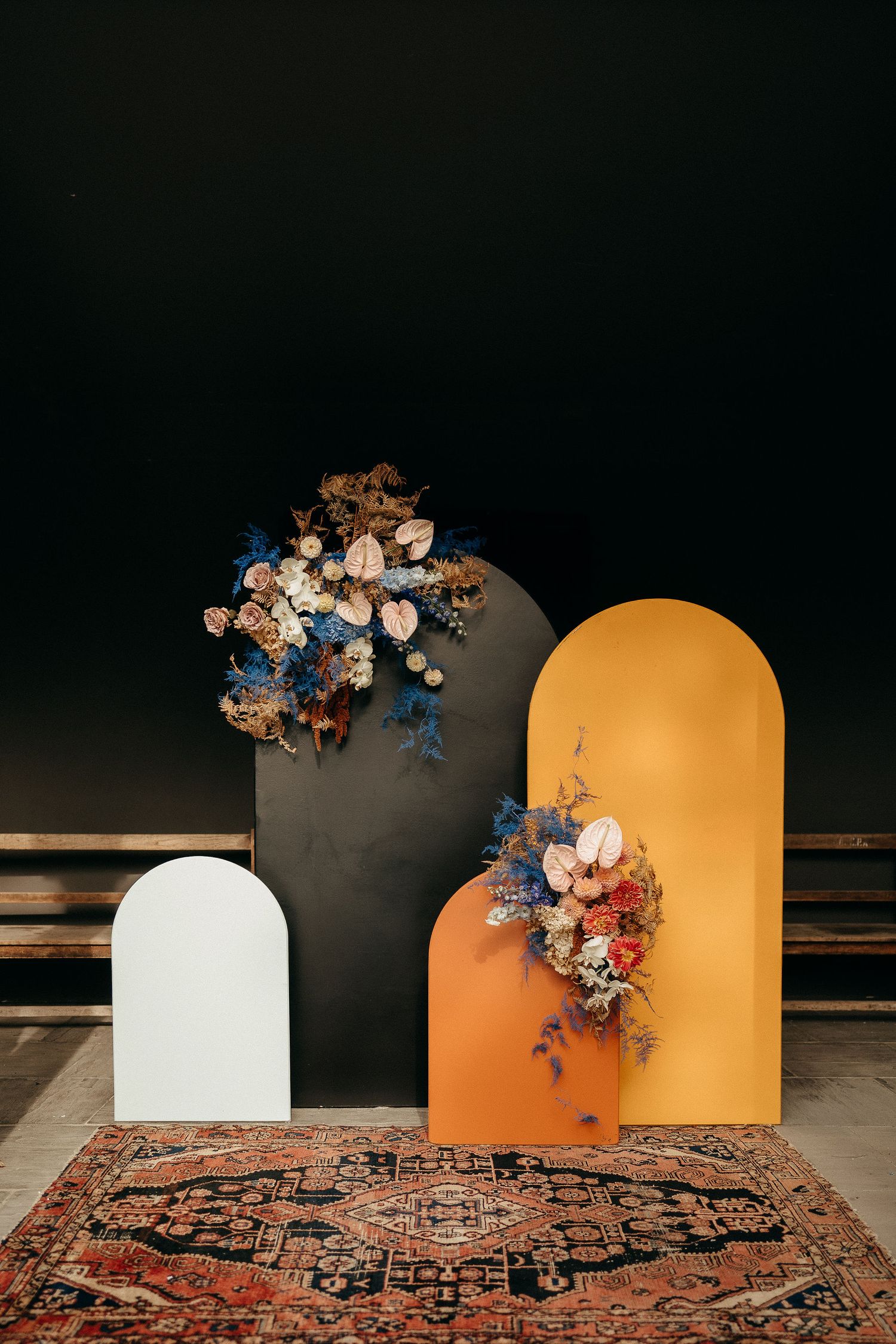 Modern arch-shaped backdrops in black, orange and white with dried floral arrangements on a vintage patterned rug.