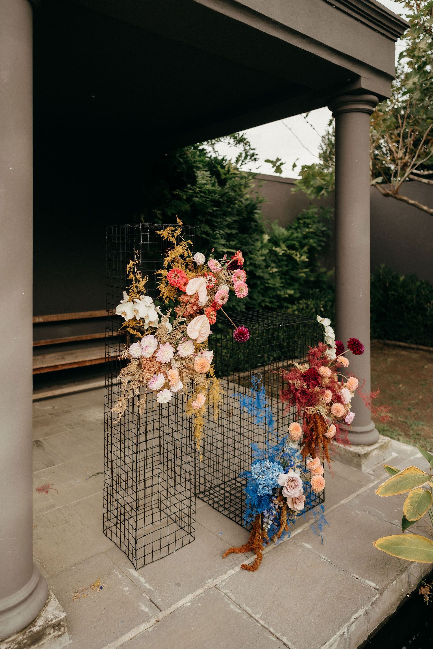 Artistic floral arrangement with pink and peach blooms adorning a wire mesh display stand on a covered porch.