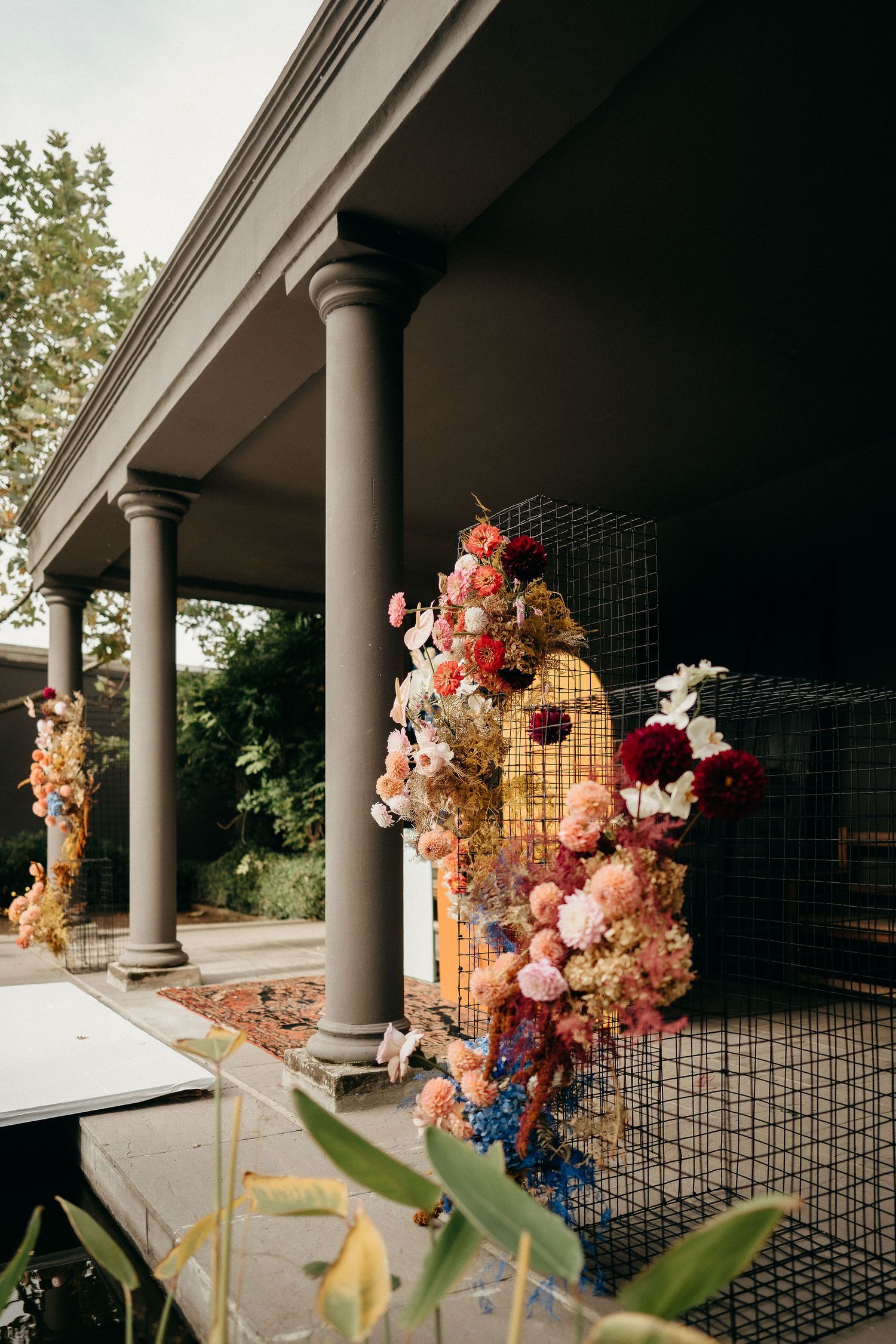 Beautiful floral arrangement with pink and orange blooms cascading along wire mesh panels on an elegant columned porch.