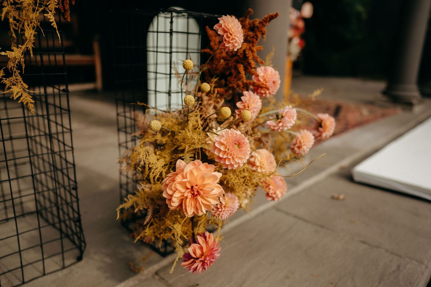 Dried autumn-colored flowers arranged in a rustic bouquet with peachy dahlias and golden dried foliage on a concrete surface.