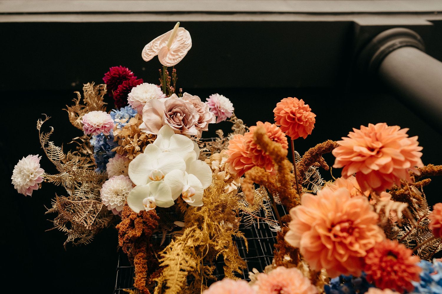 Beautiful floral arrangement featuring coral dahlias, white orchids, and dried golden foliage in warm autumn colors.