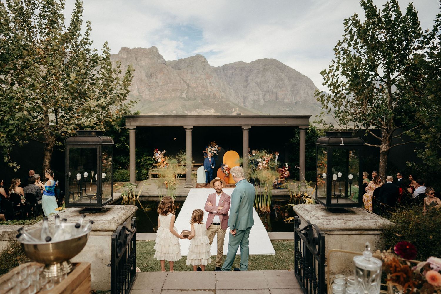 A rustic mountain wedding ceremony takes place at an outdoor venue with dramatic peaks in the background.