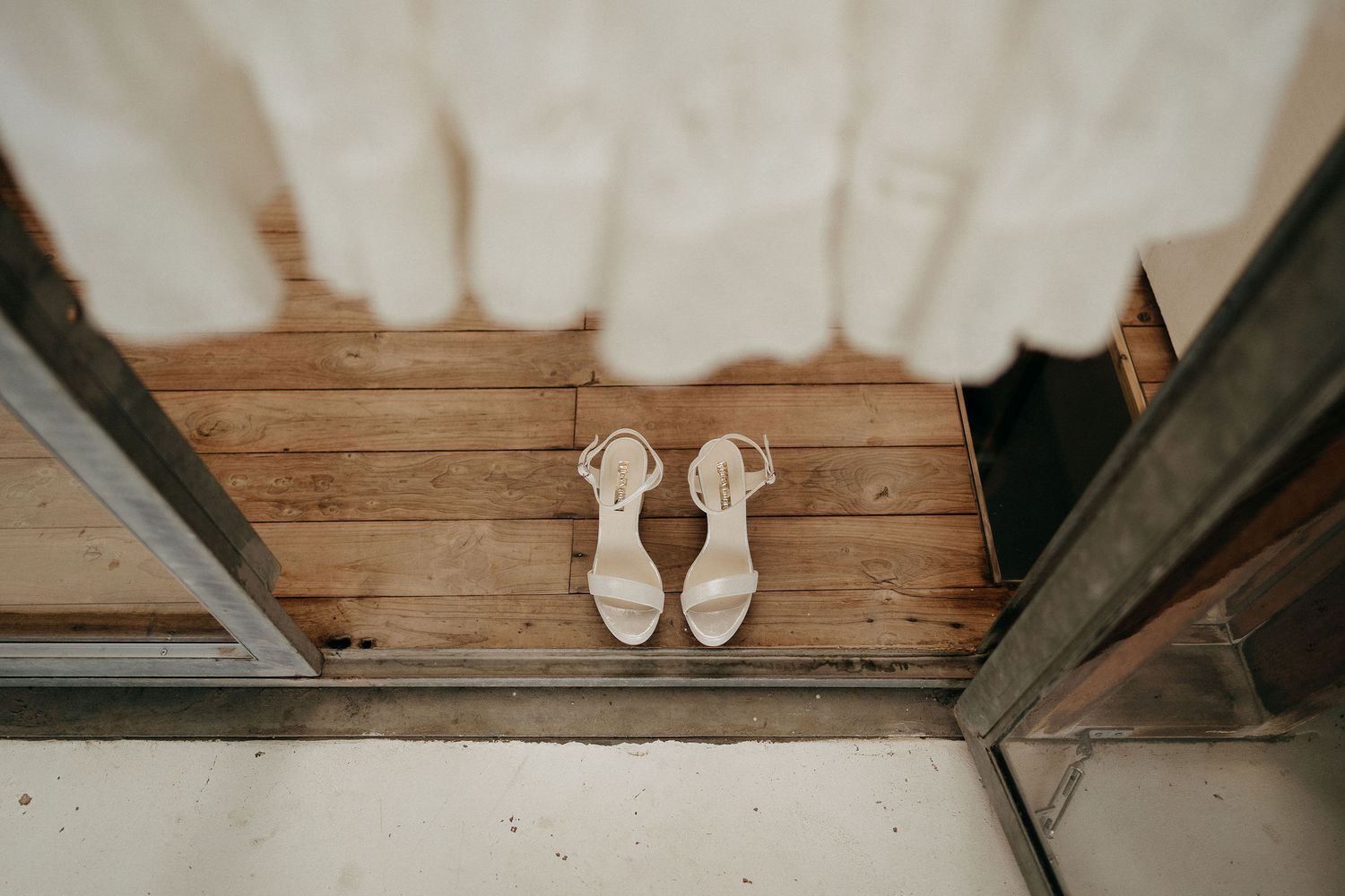White bridal shoes sitting on wooden floorboards next to a doorway in a minimalist wedding detail photo.