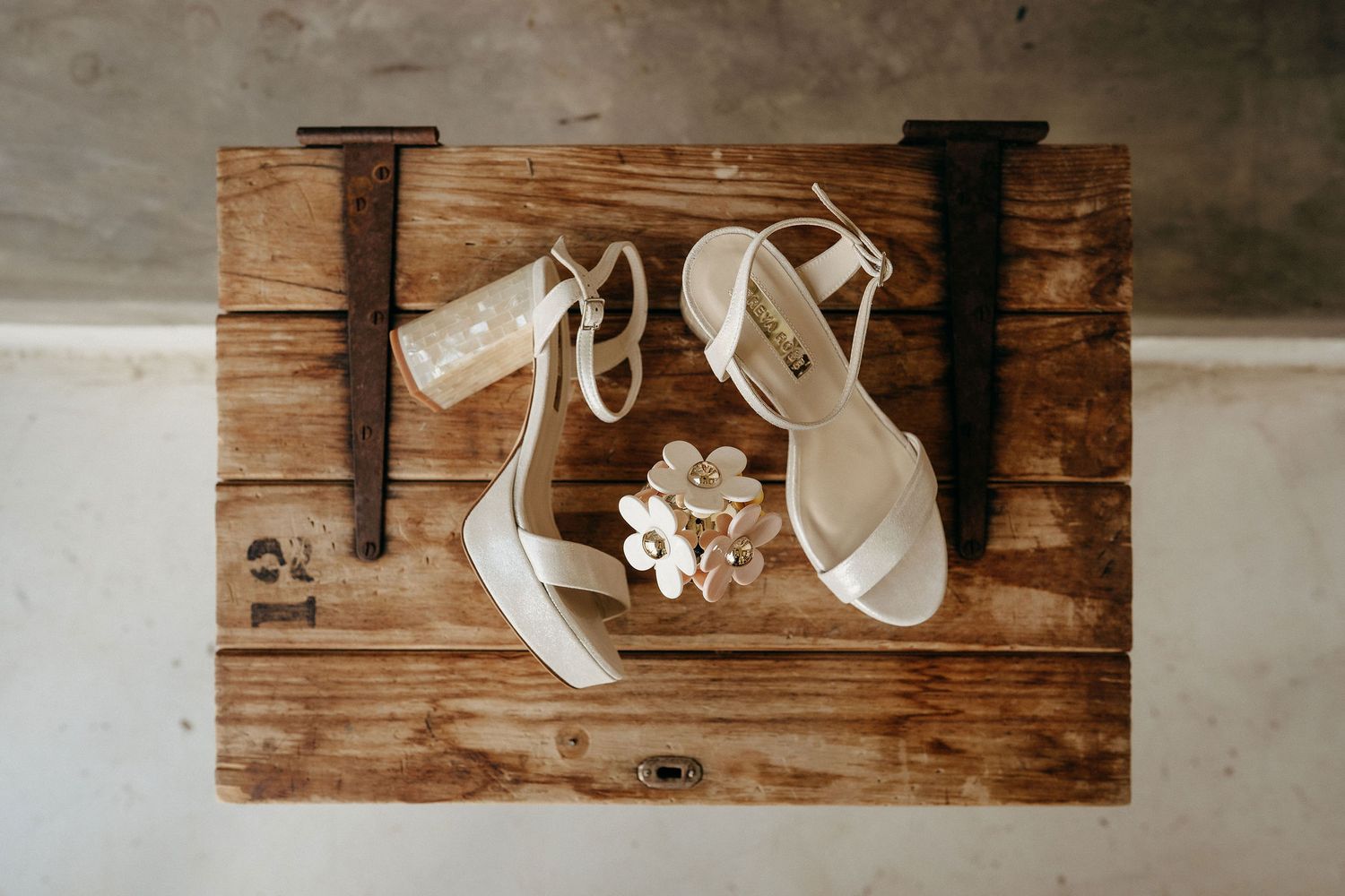 White wedding heels and small bouquet arranged on rustic wooden surface with black wall hooks.