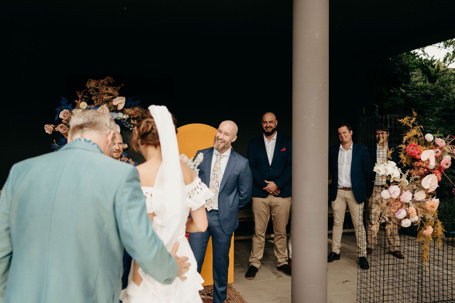 A special moment captured at an outdoor wedding ceremony with floral decorations and a white pillar in the foreground.