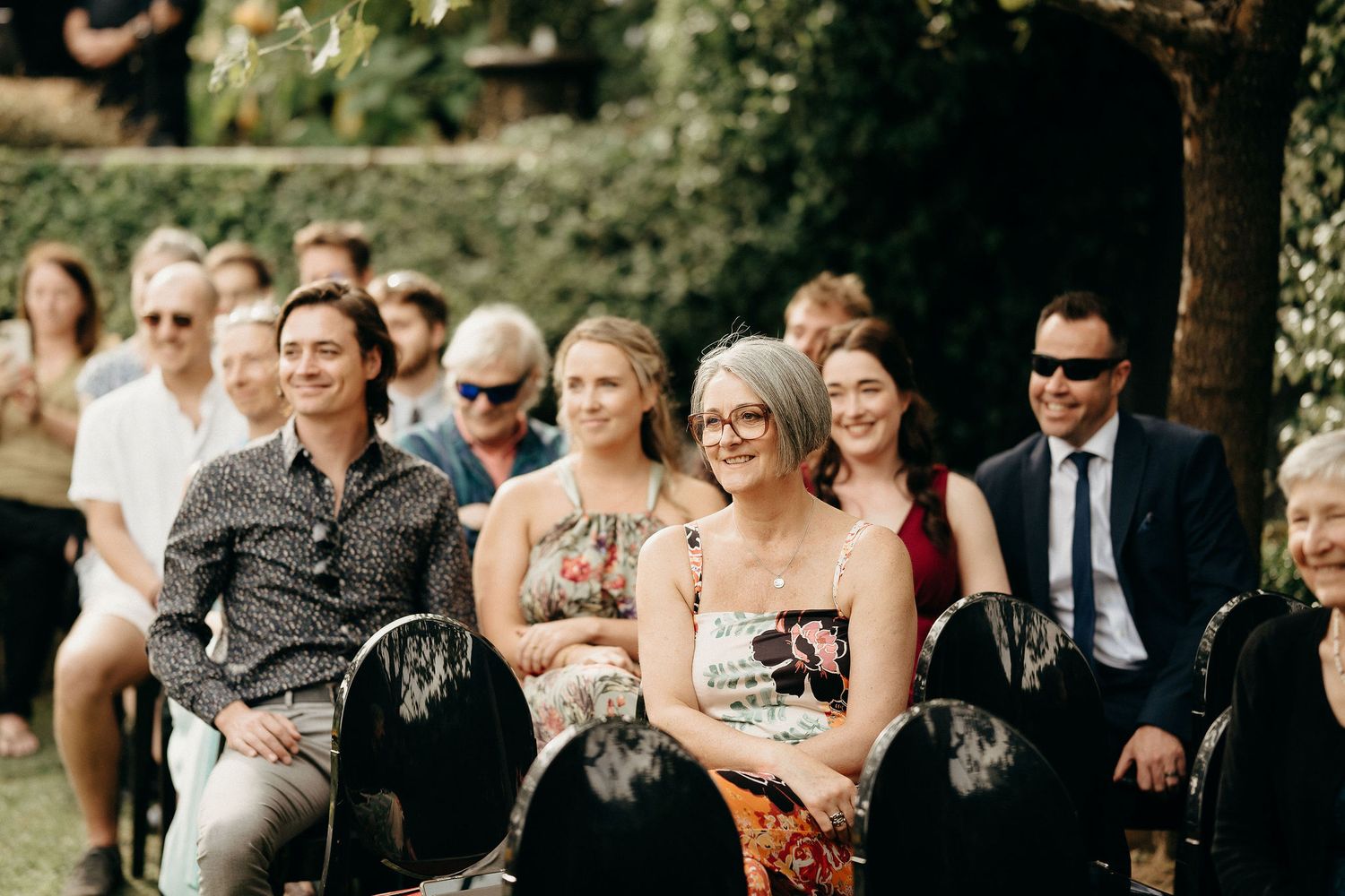 Wedding guests seated outdoors in a garden setting watching a ceremony during a summer event.