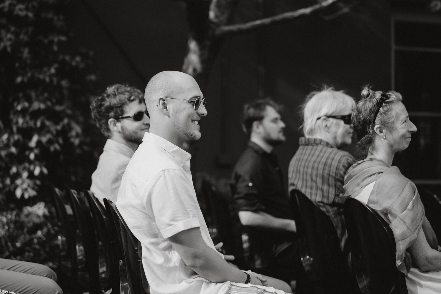 A black and white profile shot of people sitting in a row outdoors.