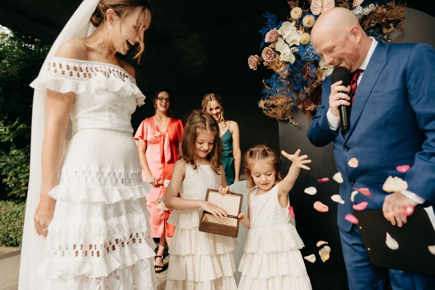 A wedding celebration outdoors with falling rose petals and a decorative floral arch.