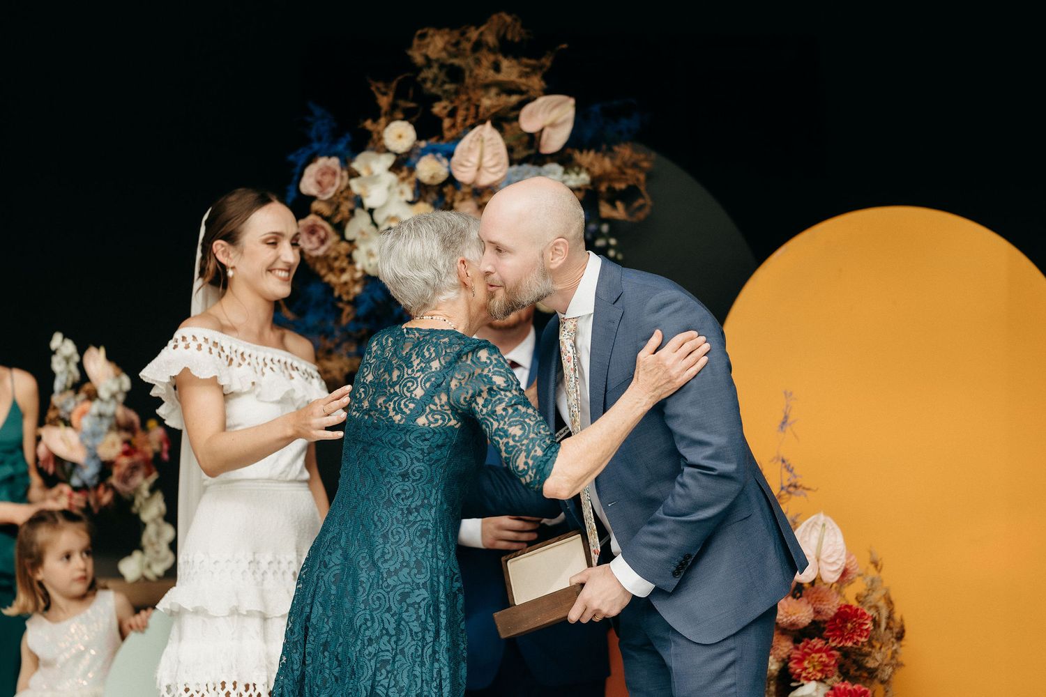 Wedding celebration moment with guests sharing joyful emotions against a floral backdrop.
