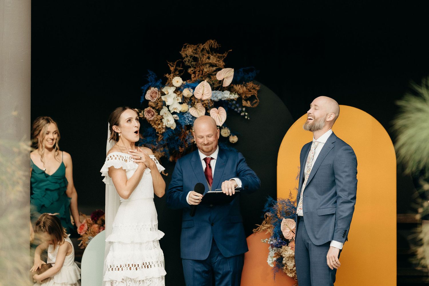 Wedding ceremony takes place in front of a modern arch with dried floral arrangements and a yellow circular backdrop.