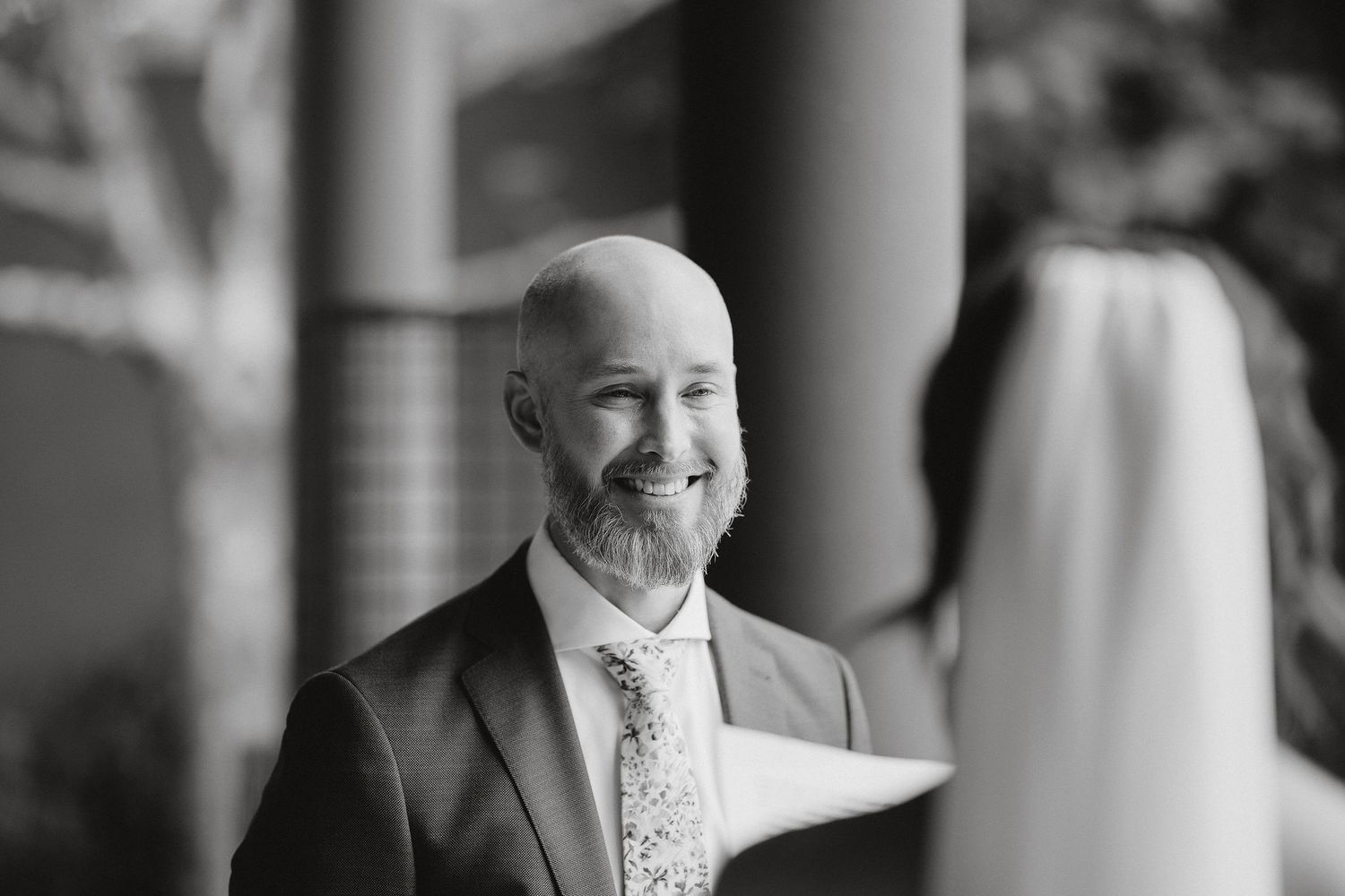 Black and white photo of groom in suit smiling during wedding first look moment.