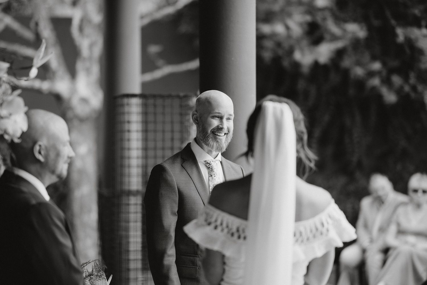 Black and white photo of a joyful wedding ceremony moment showing emotional reactions during the vows at an outdoor venue.