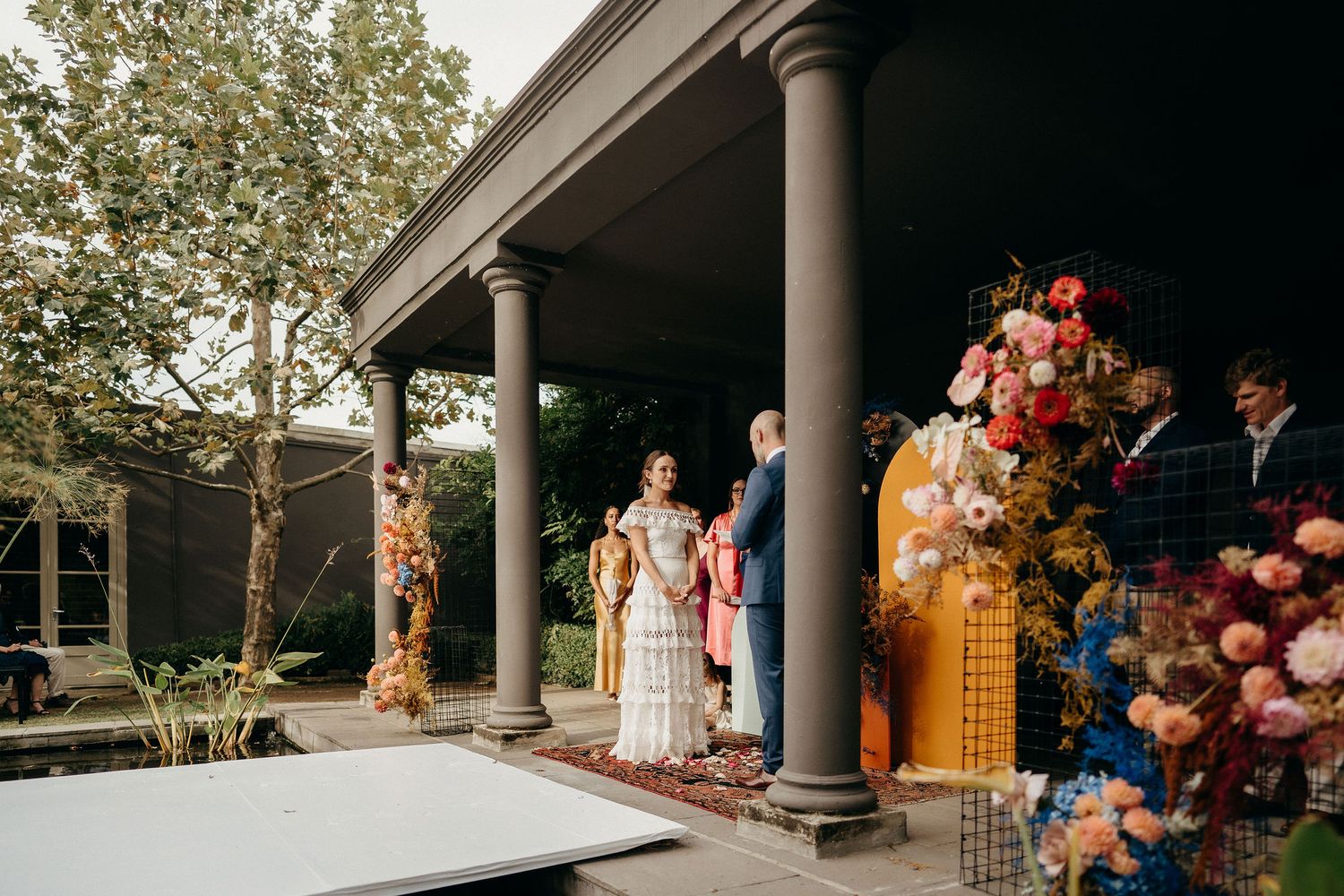 Wedding ceremony setup with columns and colorful balloon arrangements under an outdoor pavilion.