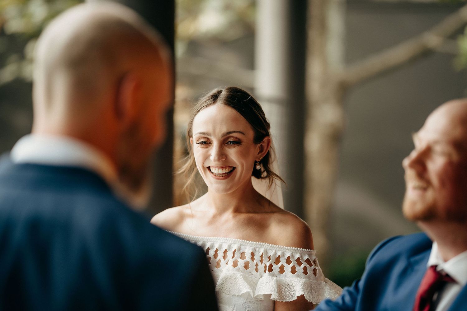 A joyful moment during a wedding ceremony with attendees dressed in blue suits and a white off-shoulder dress.