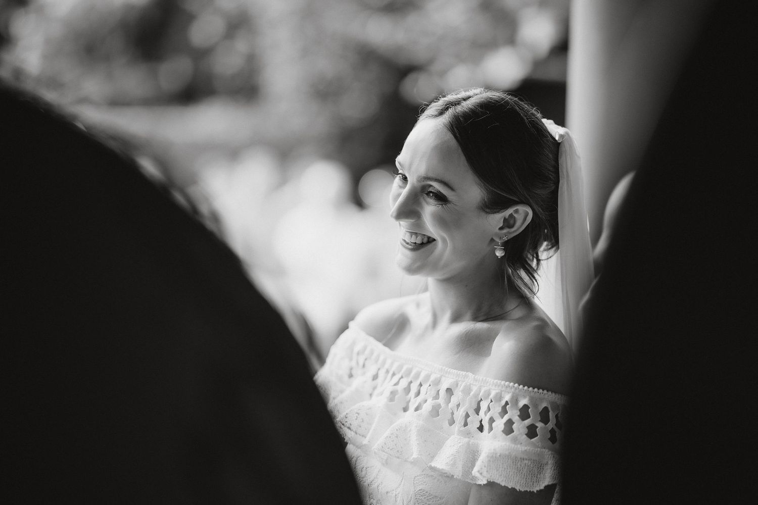 Black and white portrait of bride in off-shoulder wedding dress smiling while looking to the side.