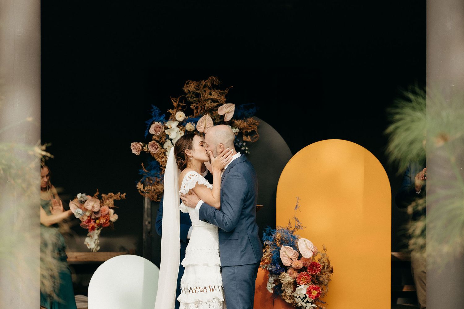 A wedding couple sharing a romantic moment under an arch decorated with floral arrangements and balloons.