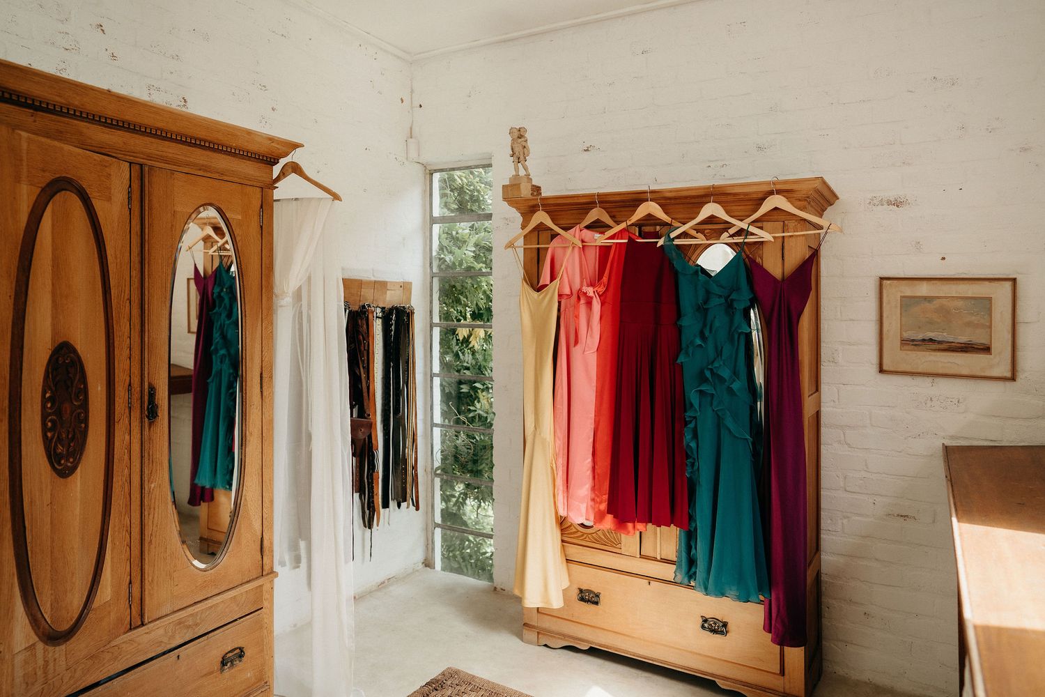 Colorful dresses hanging in a bright dressing room with wooden wardrobe and natural light from window.